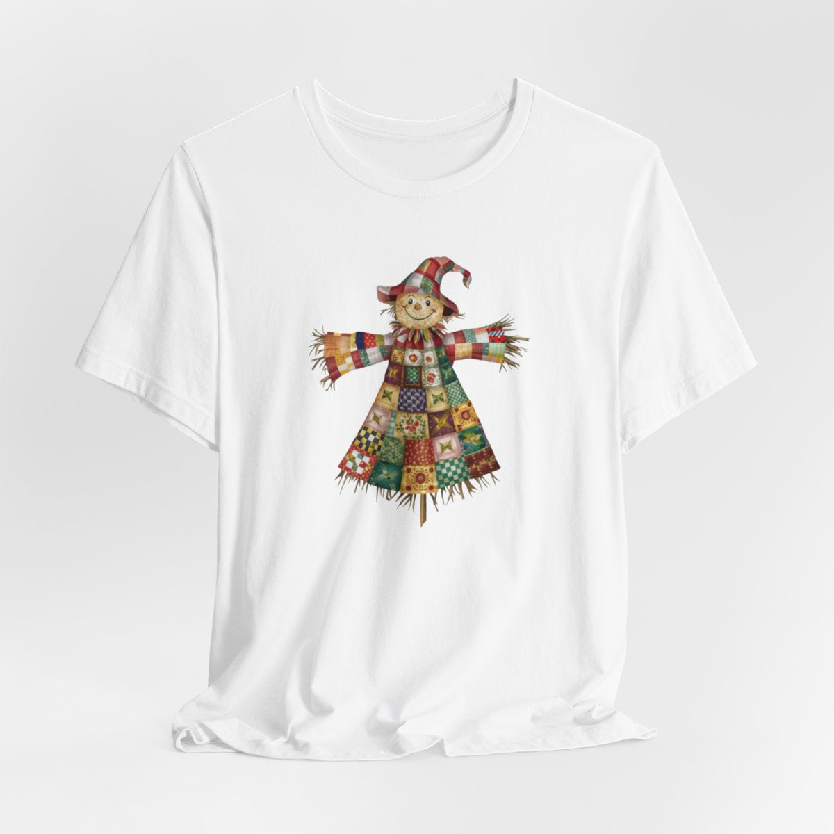 A White thanksgiving  quilting t-shirt featuring a smiling scarecrow made entirely of colorful quilt patterns. Wearing a patchwork hat and clothes with various quilt designs. Straw details on hands and neck. Cheerful autumn-themed illustration celebrating quilting craft.