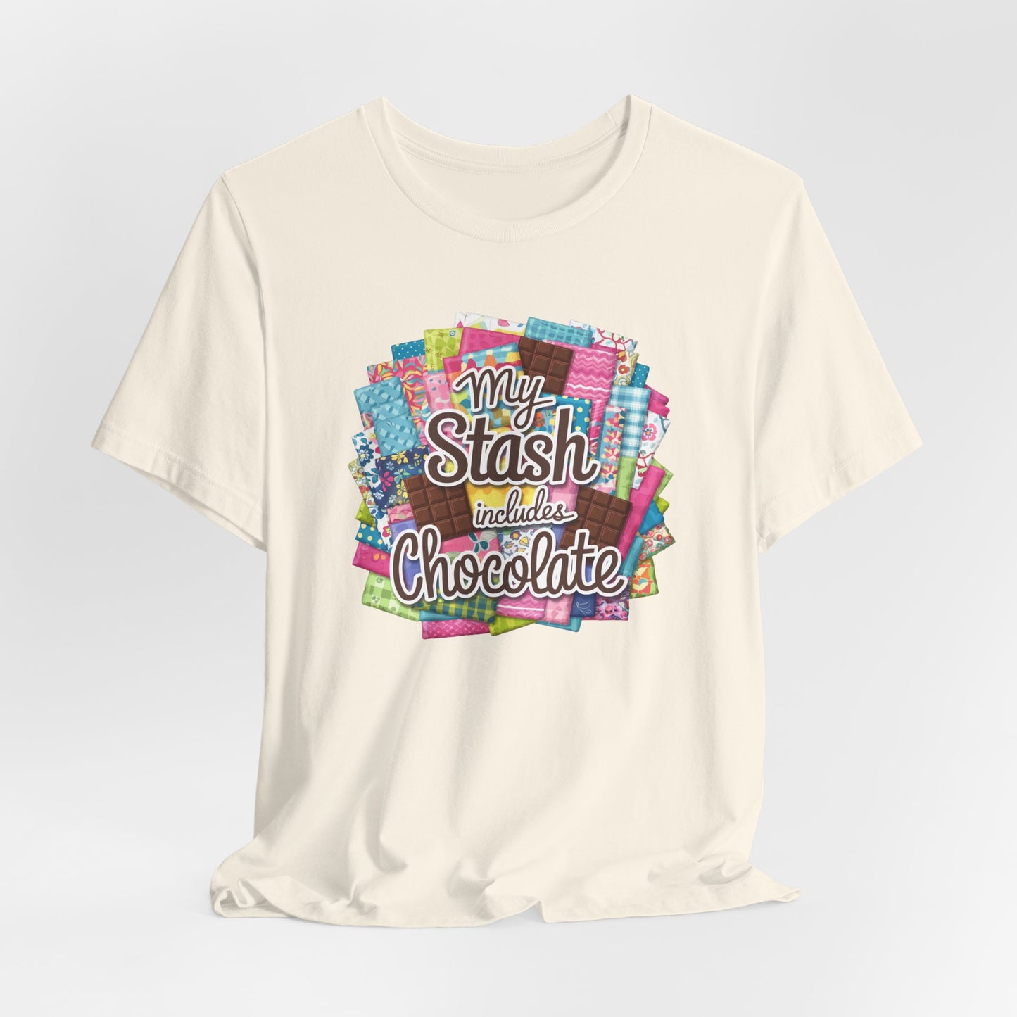 A Natural t-shirt featuring a colorful design of a fabric stash mixed with chocolate bars and the phrase 'My Stash Includes Chocolate,' perfect for quilters and chocolate lovers