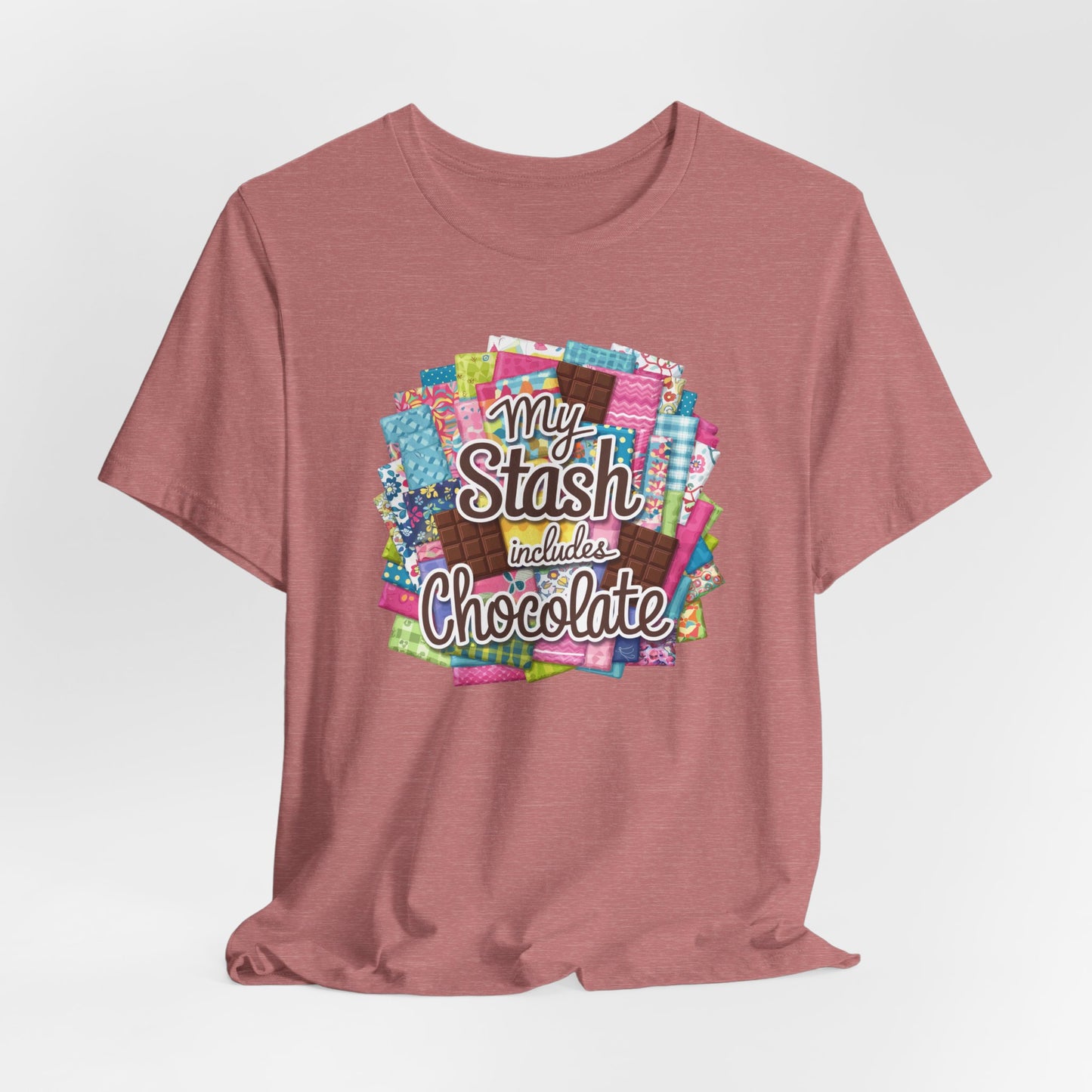 A Heather Mauve t-shirt featuring a colorful design of a fabric stash mixed with chocolate bars and the phrase 'My Stash Includes Chocolate,' perfect for quilters and chocolate lovers