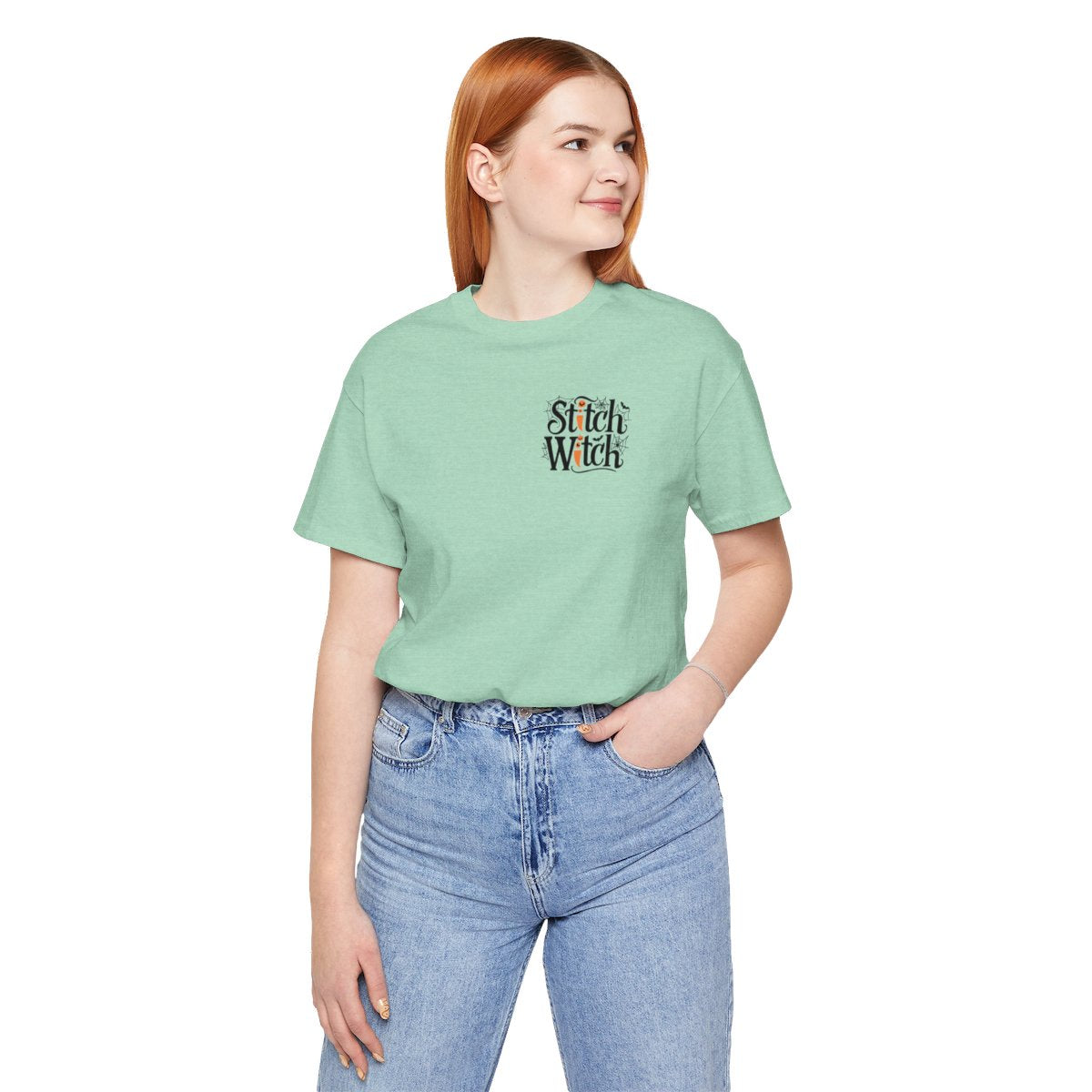 A Heather Mint Halloween Quilting T-Shirt featuring "Stitch Witch" text in Halloween-themed typography. Jack-o'-lanterns, spiderwebs, and bats decorate the letters. The "i" in "Stitch" resembles a sewing needle. Ideal for quilters who love Halloween.