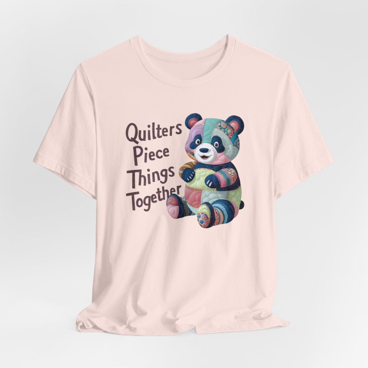 A Soft Pink fun T-Shirt with the phrase Quilters Piece Things Together with a patchwork panda design . The panda is made of colorful fabric scraps stitched together, creating a whimsical and crafty appearance. Perfect for quilting enthusiasts with a sense of humor.