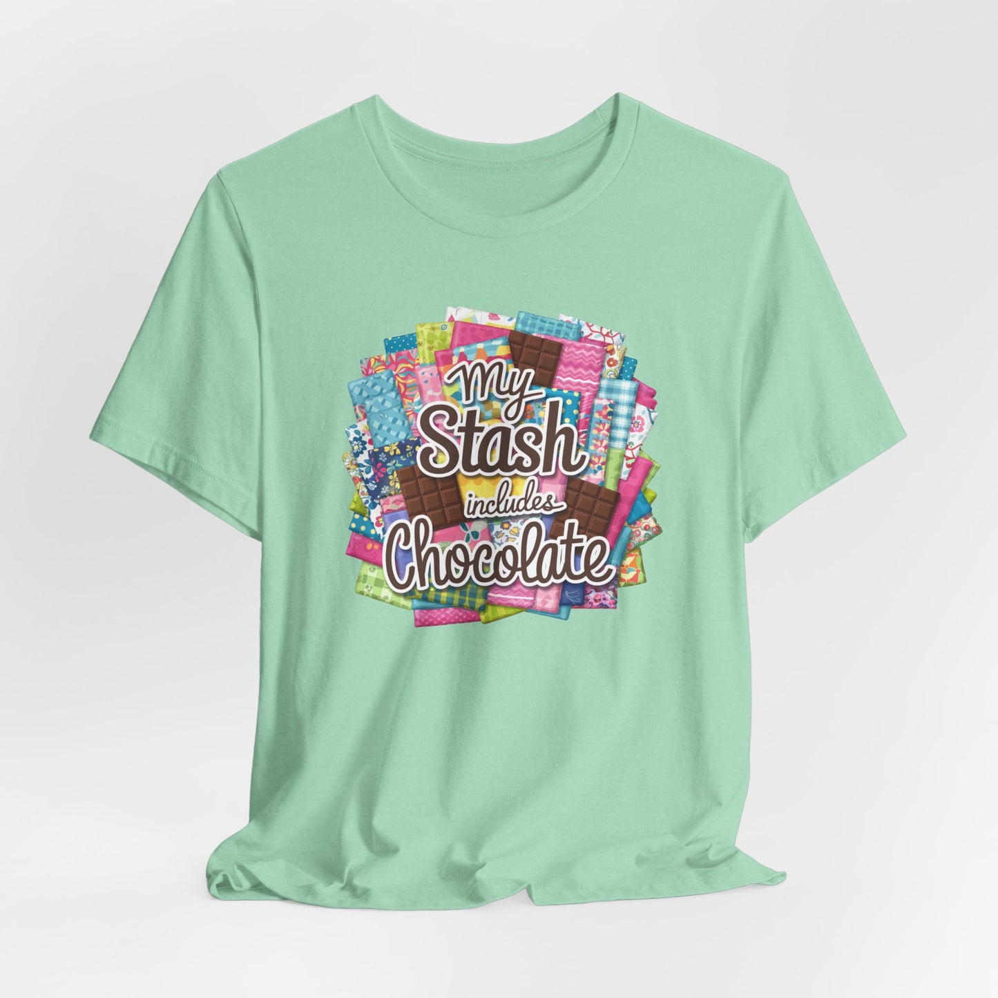 A Heather Mint t-shirt featuring a colorful design of a fabric stash mixed with chocolate bars and the phrase 'My Stash Includes Chocolate,' perfect for quilters and chocolate lovers