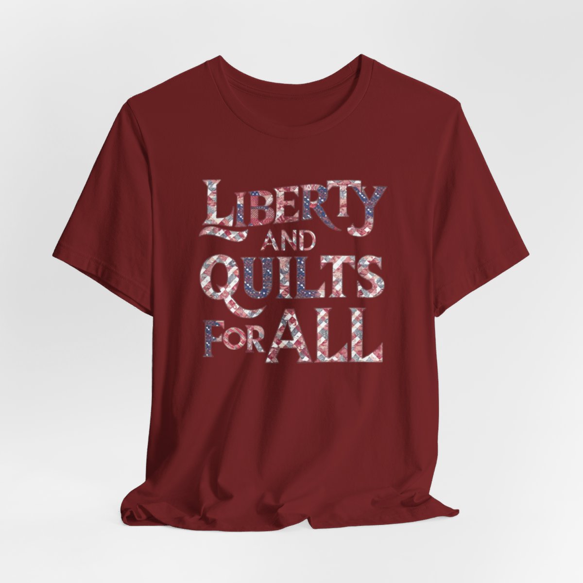 A Cardinal T-shirt featuring text "LIBERTY AND QUILTS FOR ALL" in large decorative letters filled with various quilt patterns in red, white, and blue.