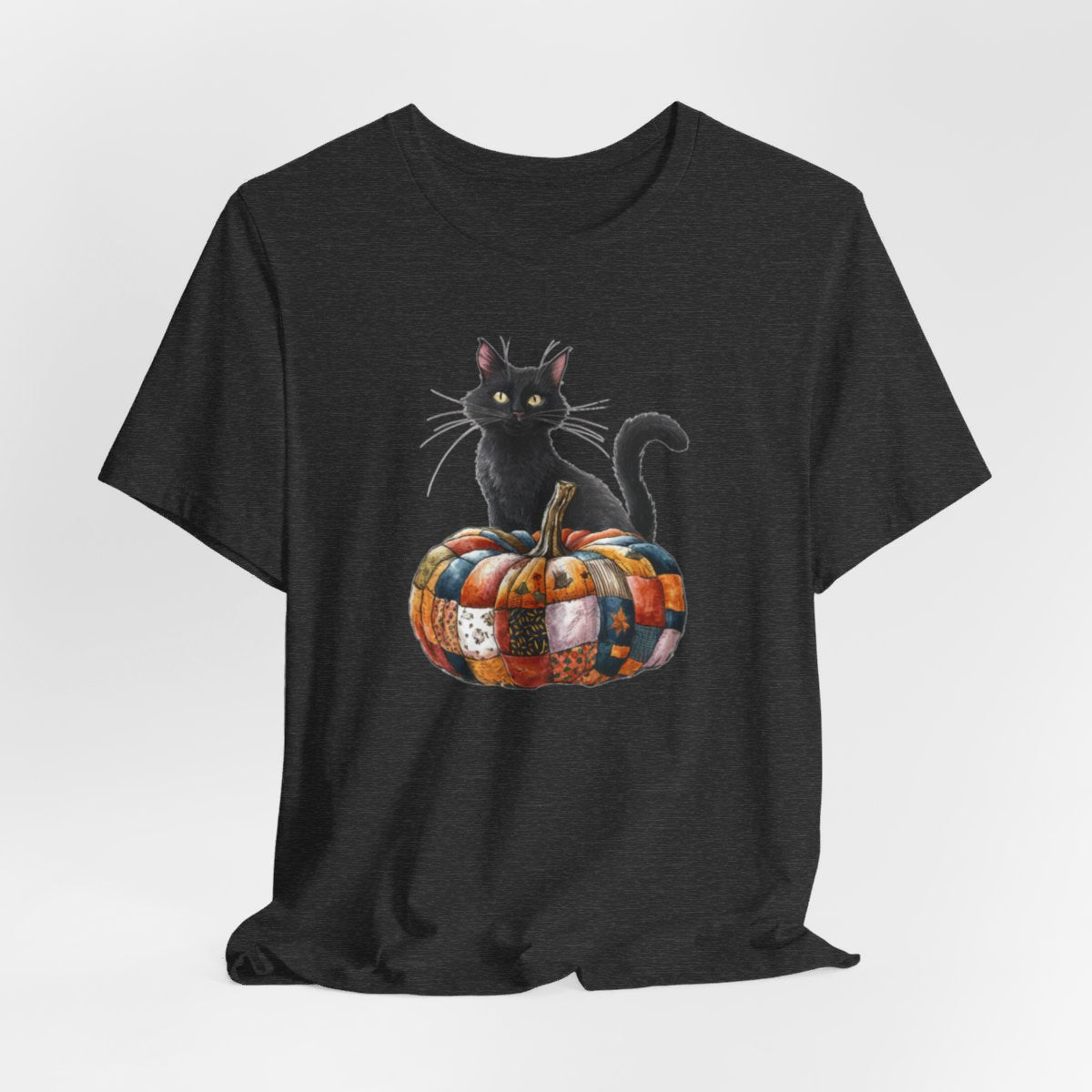 A Dark Grey Heather Halloween Quilting T-Shirt featuring a black cat sitting on colorful patchwork quilt pumpkin. Cat has yellow eyes and long whiskers. Pumpkin features various quilt patterns in autumn colors. Halloween-themed t-shirt design for quilting enthusiasts.