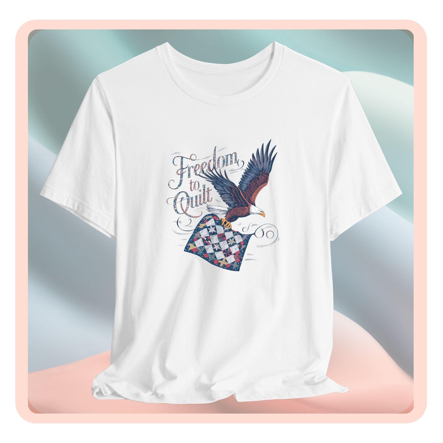 A T-shirt with detailed illustration of a bald eagle in flight, carrying a patchwork quilt. Text reads "Freedom to Quilt" in an ornate, patriotic font.