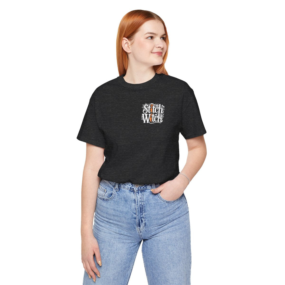 A Dark Grey Heather Halloween Quilting T-Shirt featuring "Stitch Witch" text in Halloween-themed typography. Jack-o'-lanterns, spiderwebs, and bats decorate the letters. The "i" in "Stitch" resembles a sewing needle. Ideal for quilters who love Halloween.