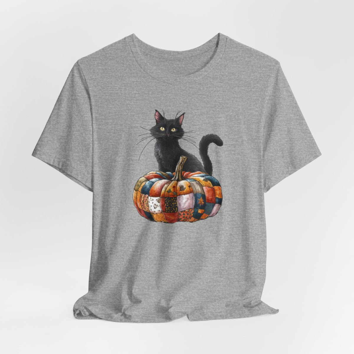 An Athletic Heather Halloween Quilting T-Shirt featuring a black cat sitting on colorful patchwork quilt pumpkin. Cat has yellow eyes and long whiskers. Pumpkin features various quilt patterns in autumn colors. Halloween-themed t-shirt design for quilting enthusiasts.