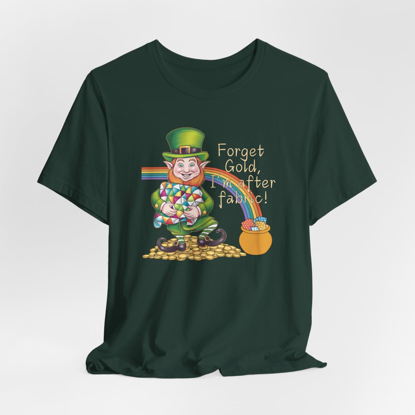 A Forest short-sleeve t-shirt featuring a cheerful leprechaun holding a quilt, sitting on gold coins, with a rainbow leading to a fabric-filled pot and the phrase 'Forget Gold, I’m After Fabric!' Perfect for quilters celebrating St. Patrick’s Day.