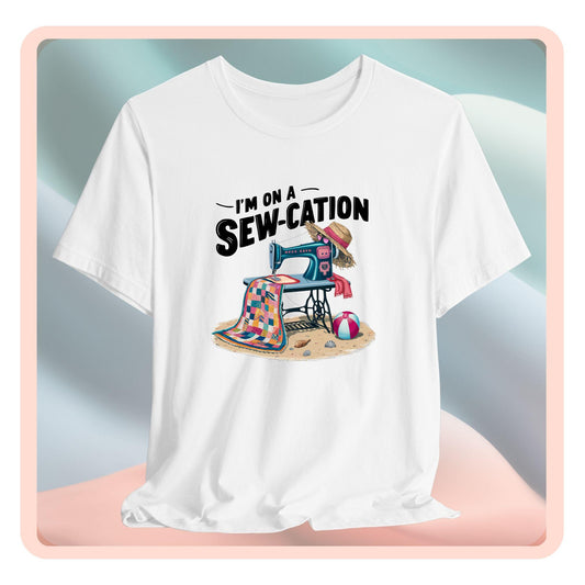 A fun Quilting T-shirt of a vintage sewing machine on a beach with a colorful quilt, sun hat, and beach ball. Text above reads "I'm on a Sew-cation" in bold letters.