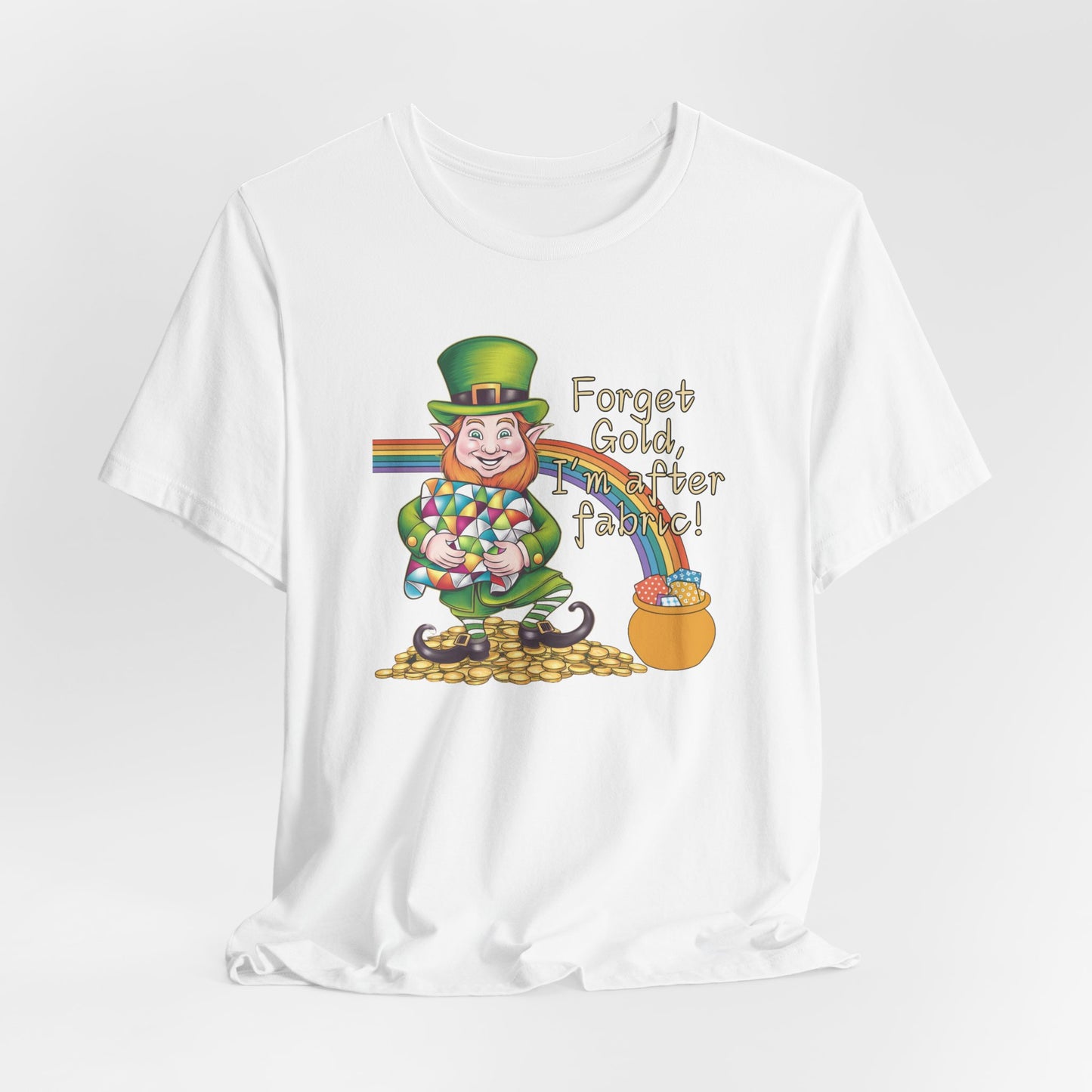 A White short-sleeve t-shirt featuring a cheerful leprechaun holding a quilt, sitting on gold coins, with a rainbow leading to a fabric-filled pot and the phrase 'Forget Gold, I’m After Fabric!' Perfect for quilters celebrating St. Patrick’s Day.