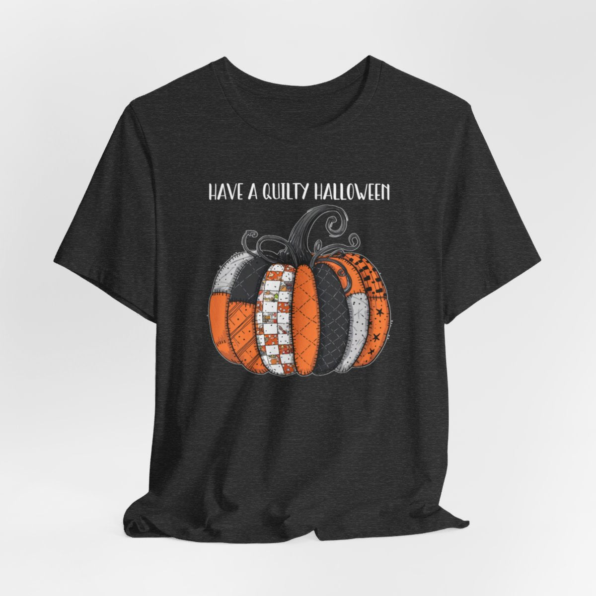 A Dark Grey Heather Halloween Quilting T-Shirt featuring patchwork pumpkin with various quilt patterns. Mix of Halloween and traditional quilt motifs. Intricate stitching details. Text reads "Have a Quilty Halloween". Ideal for quilters who love Halloween.