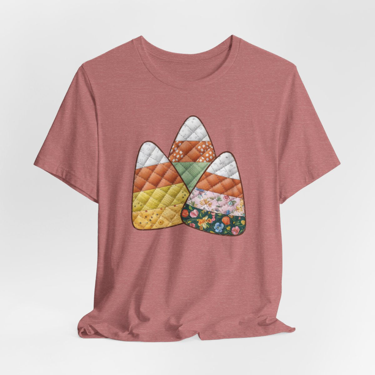 A Heather Mauve Halloween Quilting T-Shirt featuring three large candy corn shapes made of quilted fabrics with various patterns. Each candy corn section features different quilting motifs in autumn colors. Playful take on Halloween candy and quilting craft.