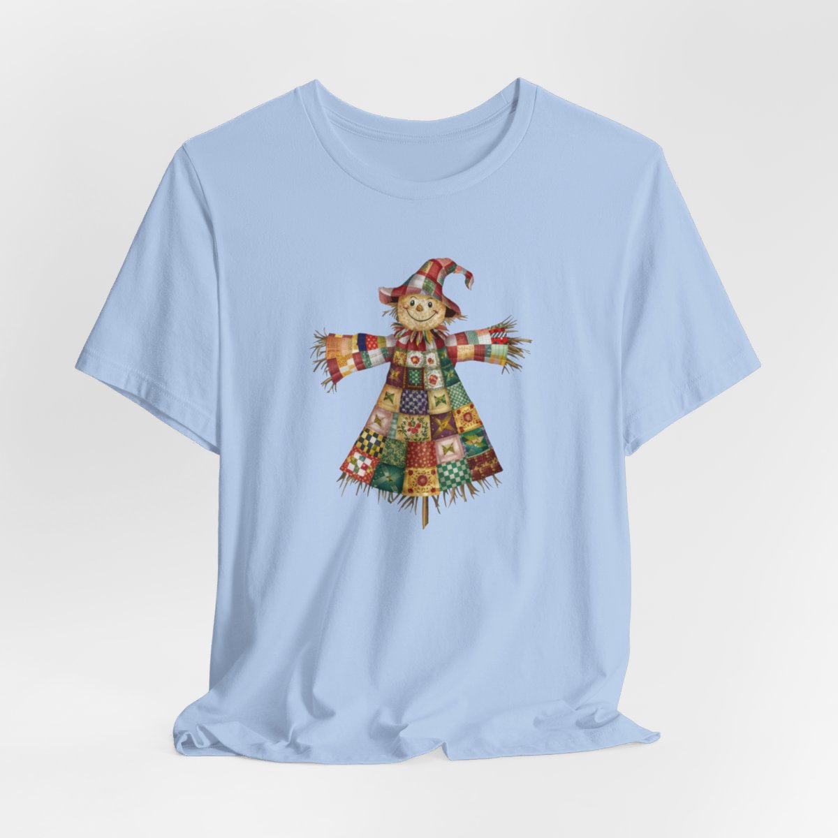 A Baby Blue thanksgiving  quilting t-shirt featuring a smiling scarecrow made entirely of colorful quilt patterns. Wearing a patchwork hat and clothes with various quilt designs. Straw details on hands and neck. Cheerful autumn-themed illustration celebrating quilting craft.