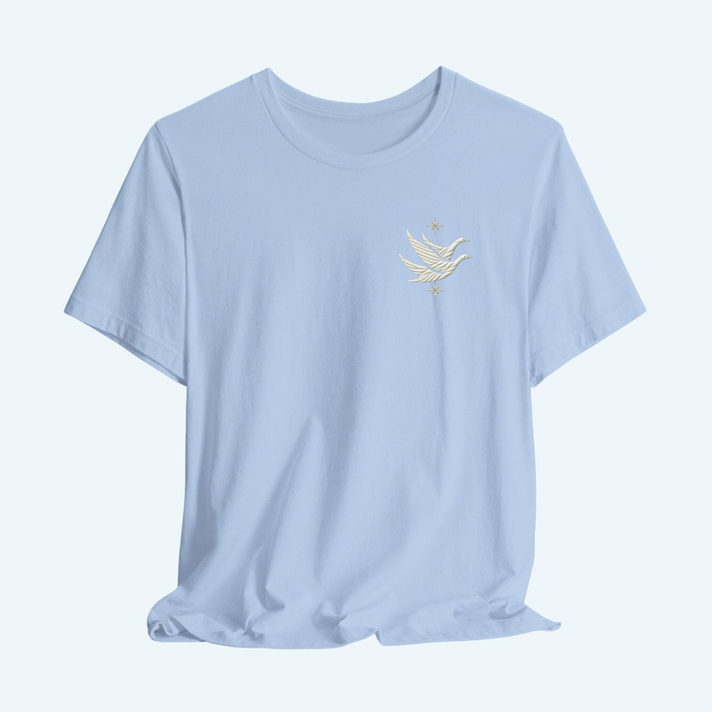 A T-shirt featuring two stylized white geese in flight, with outstretched wings. The geese are composed of intricate geometric patterns resembling quilt stitching. Two eight-pointed stars frame the scene, one above and one below the geese, adding a celestial element to the peaceful composition.