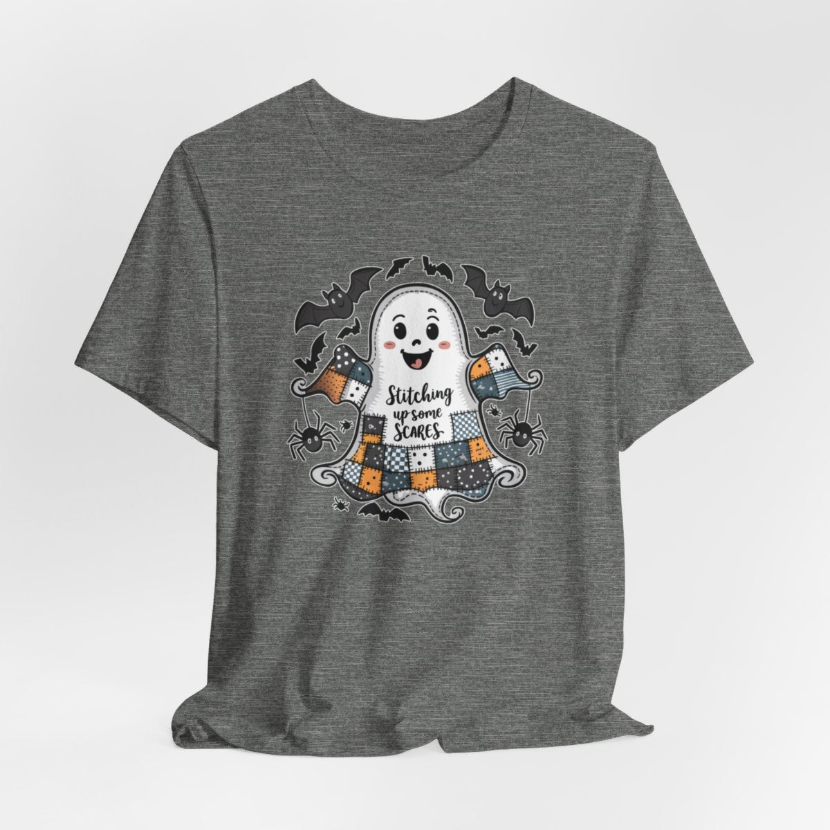 A Deep Heather Halloween Quilting T-Shirt featuring a smiling ghost with quilted patchwork body. Halloween-themed quilt patterns. Cute bats and spiders around ghost. Text reads "Stitching up some Scares". Ideal for quilters who enjoy Halloween themes.