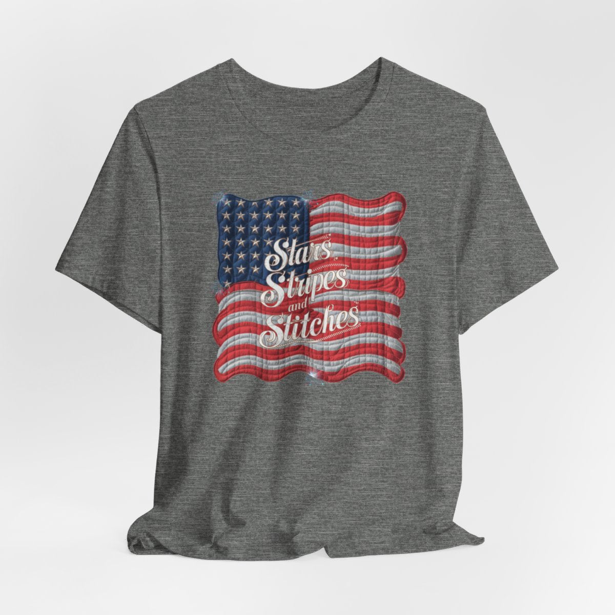 A Deep Heather T-shirt featuring quilted American flag design with text "Stars Stripes and Stitches" overlaid in stylized, patriotic font. Fireworks accent the corners.