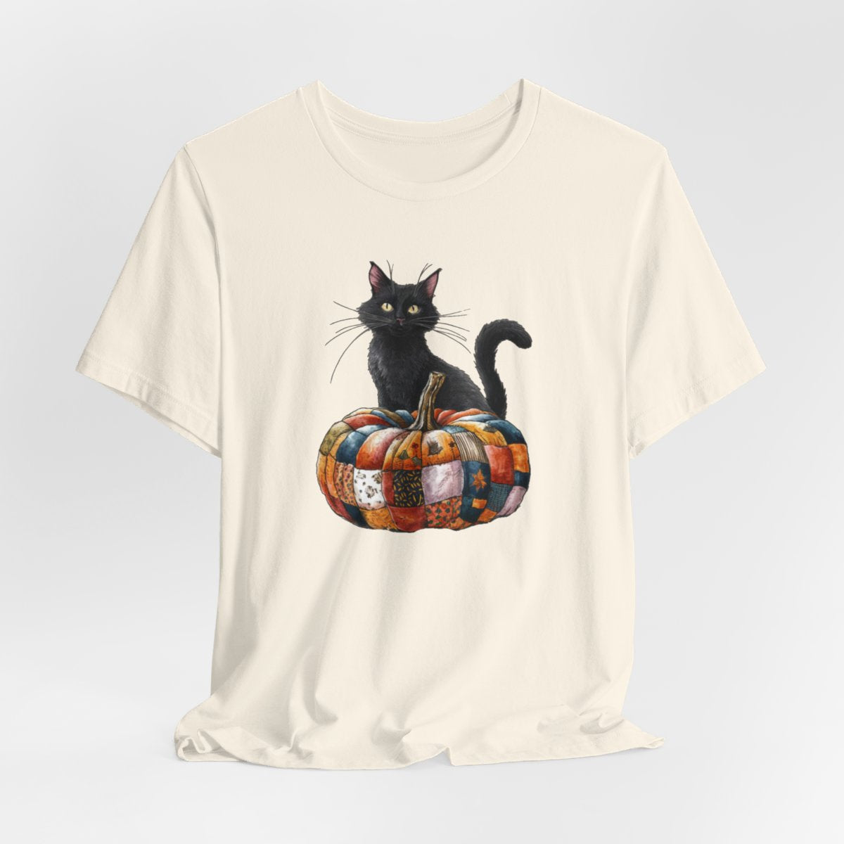 A Natural Halloween Quilting T-Shirt featuring a black cat sitting on colorful patchwork quilt pumpkin. Cat has yellow eyes and long whiskers. Pumpkin features various quilt patterns in autumn colors. Halloween-themed t-shirt design for quilting enthusiasts.