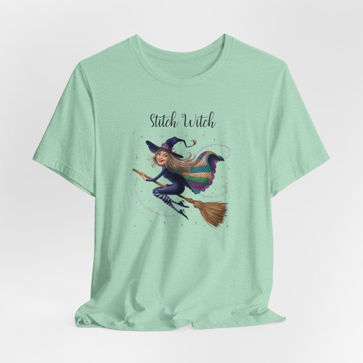 A Heather Mint Halloween Quilting T-Shirt featuring a witch riding broomstick on t-shirt design. Colorful patchwork quilt cape with various patterns. Sparkling magic and stars. Text reads "Stitch Witch". Ideal for quilters who enjoy magical themes.