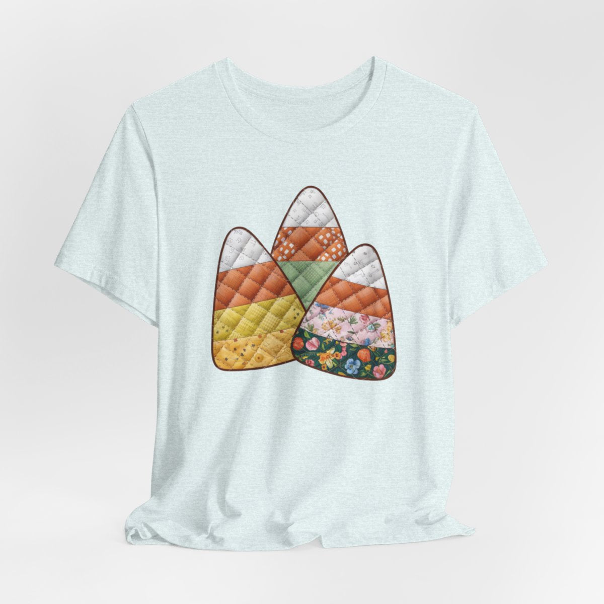 A Heather Ice Blue Halloween Quilting T-Shirt featuring three large candy corn shapes made of quilted fabrics with various patterns. Each candy corn section features different quilting motifs in autumn colors. Playful take on Halloween candy and quilting craft.