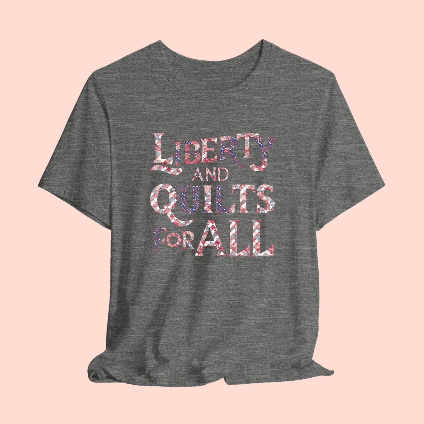 A T-shirt featuring text "LIBERTY AND QUILTS FOR ALL" in large decorative letters filled with various quilt patterns in red, white, and blue.