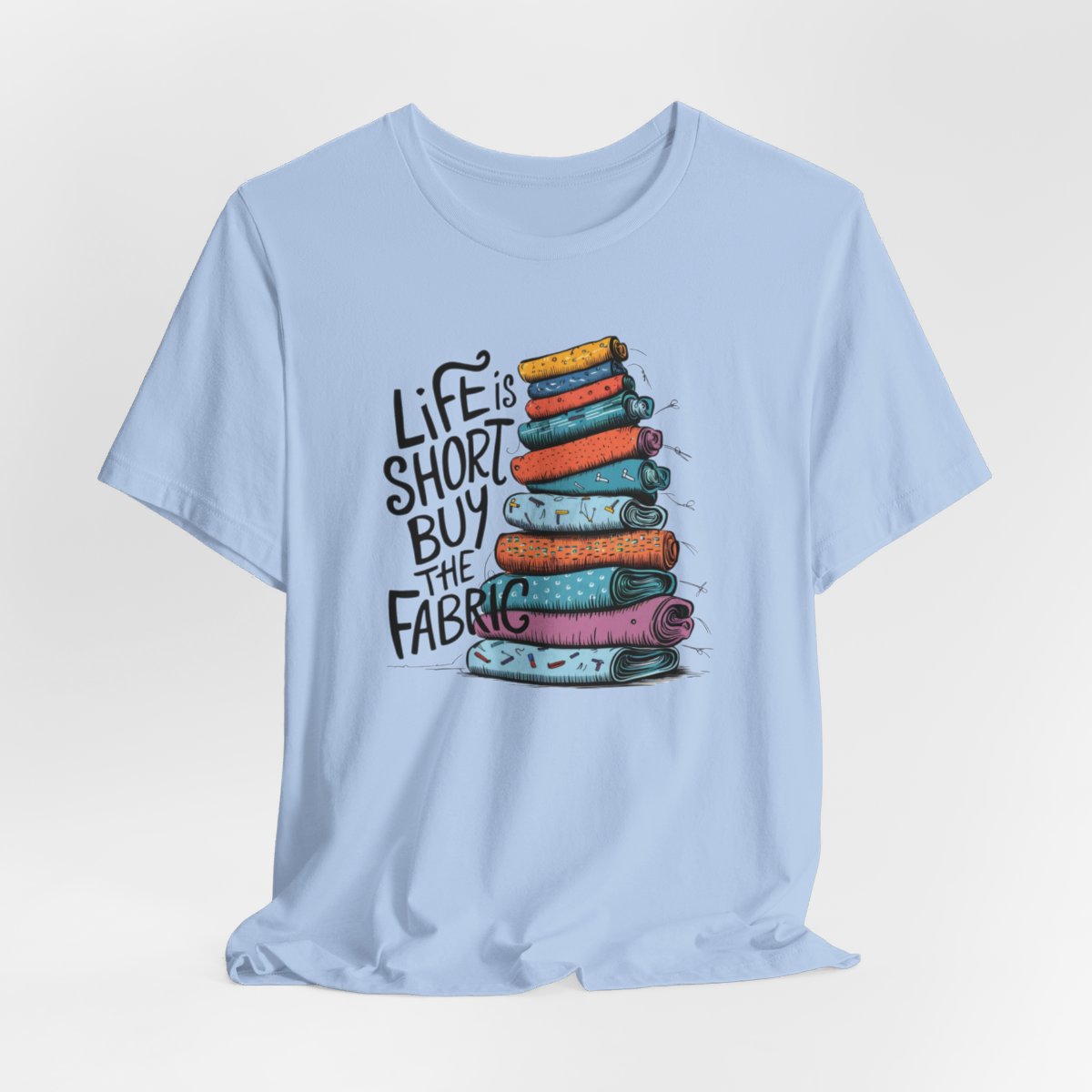 A Baby Blue fun T-Shirt with the phrase Life is Short, Buy the Fabric with the label 'Life is Short, Buy the Fabric' next to a graphic of a fun pile of fabric