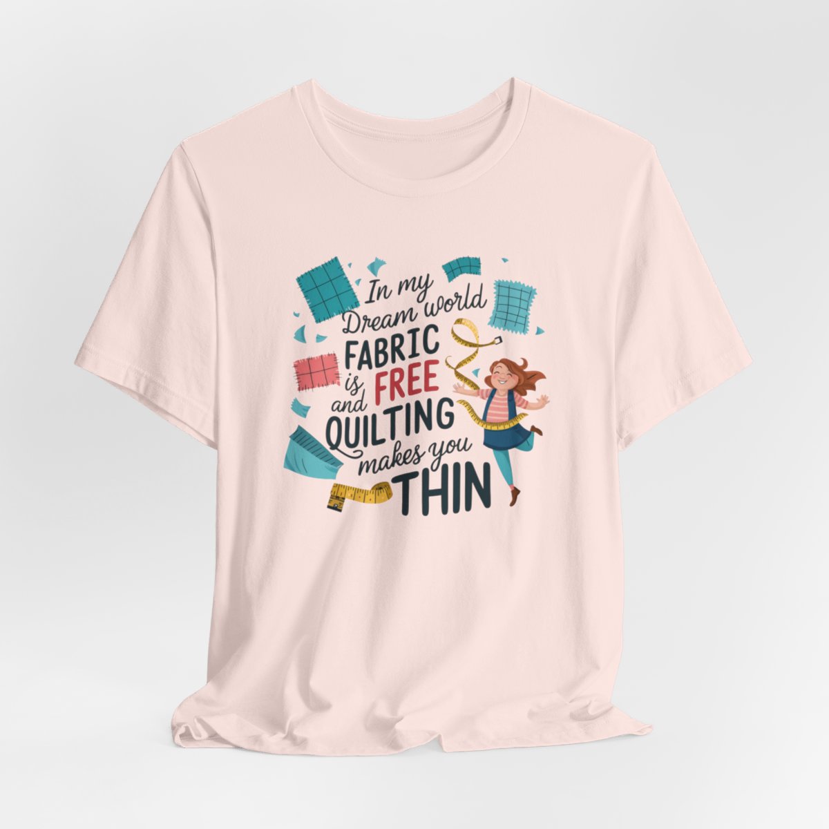 A Soft Pink funny quilting T-Shirt with the phrase Fabric is Free and Quilting Makes You Thin in a fun font with a cheerful quilter jumping for joy