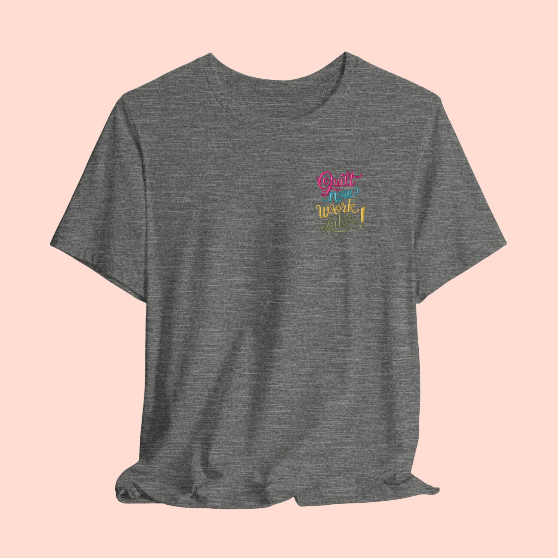 A funny quilting T-shirt featuring bold, stylized text that reads "Quilt Now, Work Later" in various vibrant colors. The playful design captures the spirit of passionate quilters who prioritize their craft over other responsibilities.