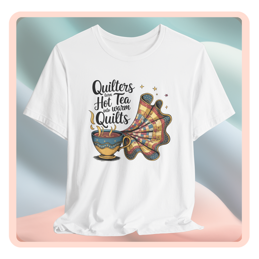 A t-shirt with a whimsical design of a teacup transforming into a patchwork quilt, accompanied by the phrase 'Quilters turn hot tea into warm quilts.' Ideal for quilters and tea lovers