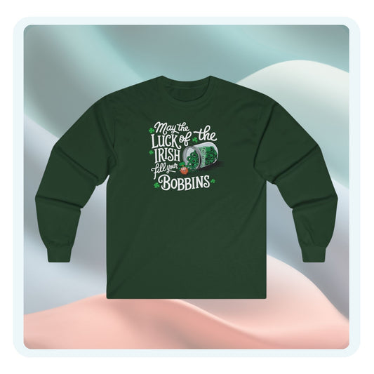 A long-sleeve t-shirt featuring a festive design with shamrocks, a spool of green thread, and the phrase 'May the Luck of the Irish Fill Your Bobbins,' perfect for quilters celebrating St. Patrick’s Day.