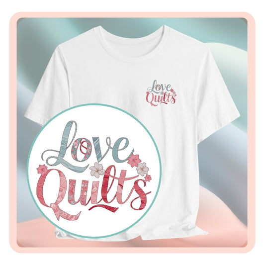 A t-shirt spelling out "Love Quilts". The word "Love" is in teal, while "Quilts" features various shades of pink and red. Small flowers in white and pink adorn the letters, creating a floral and quilting-inspired artwork.