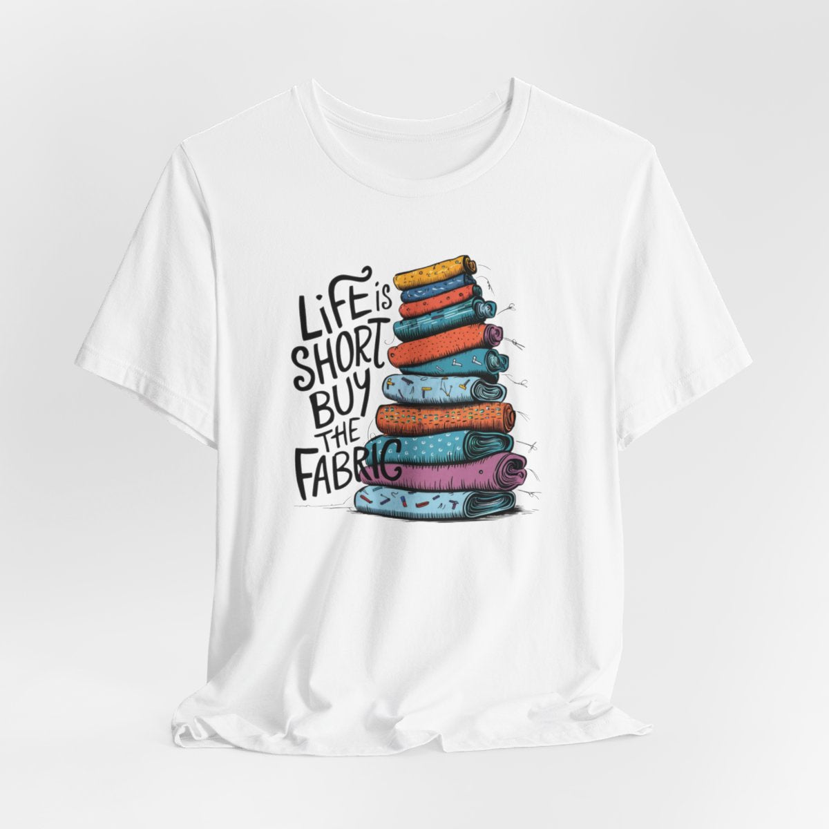 A White fun T-Shirt with the phrase Life is Short, Buy the Fabric with the label 'Life is Short, Buy the Fabric' next to a graphic of a fun pile of fabric