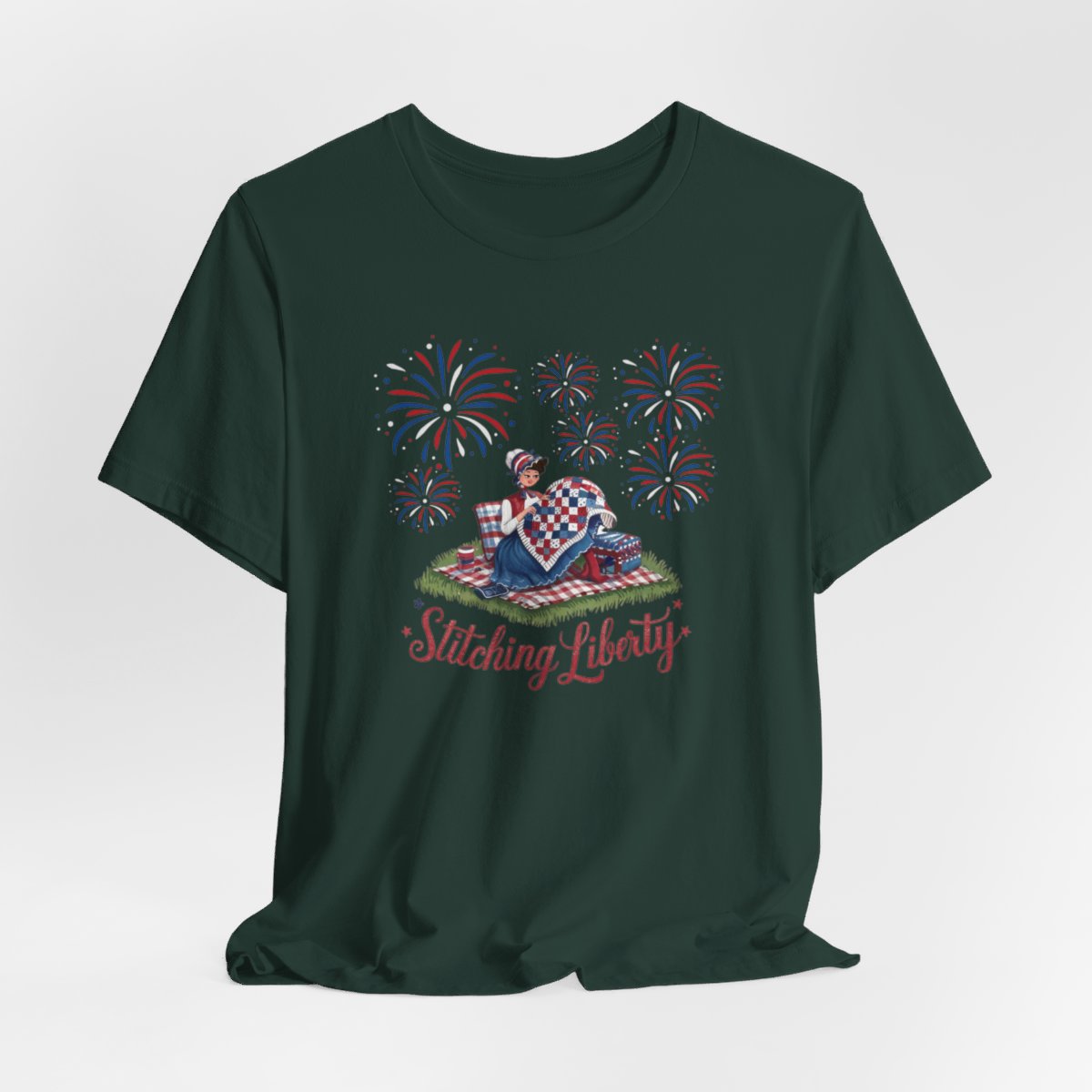 A Forest T-shirt with illustrated scene of a colonial woman quilting a patriotic blanket, surrounded by fireworks. Text reads "Stitching Liberty" in a decorative font.