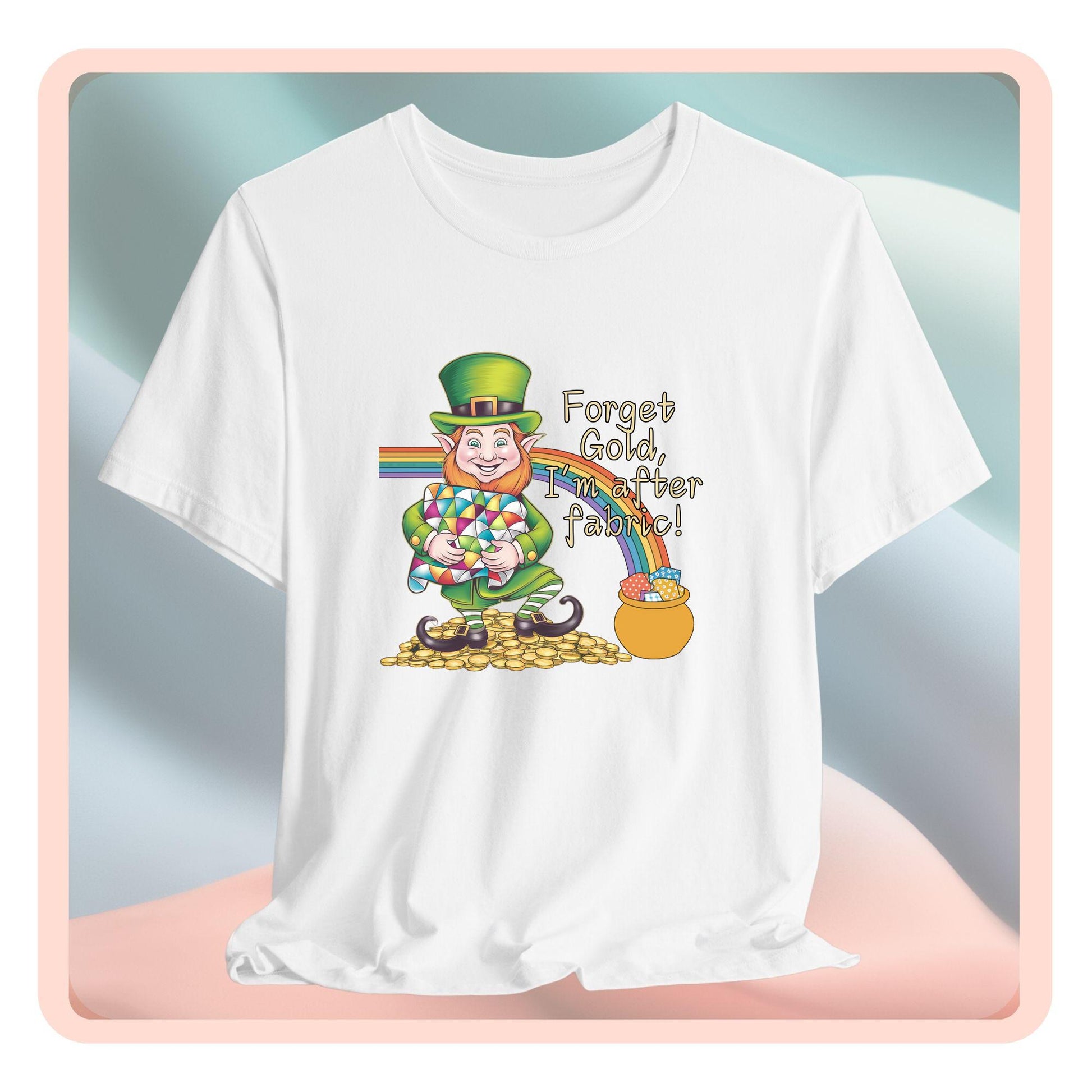 A short-sleeve t-shirt featuring a cheerful leprechaun holding a quilt, sitting on gold coins, with a rainbow leading to a fabric-filled pot and the phrase 'Forget Gold, I’m After Fabric!' Perfect for quilters celebrating St. Patrick’s Day.