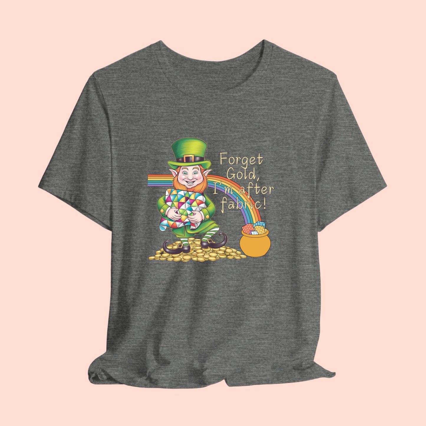 A short-sleeve t-shirt featuring a cheerful leprechaun holding a quilt, sitting on gold coins, with a rainbow leading to a fabric-filled pot and the phrase 'Forget Gold, I’m After Fabric!' Perfect for quilters celebrating St. Patrick’s Day.