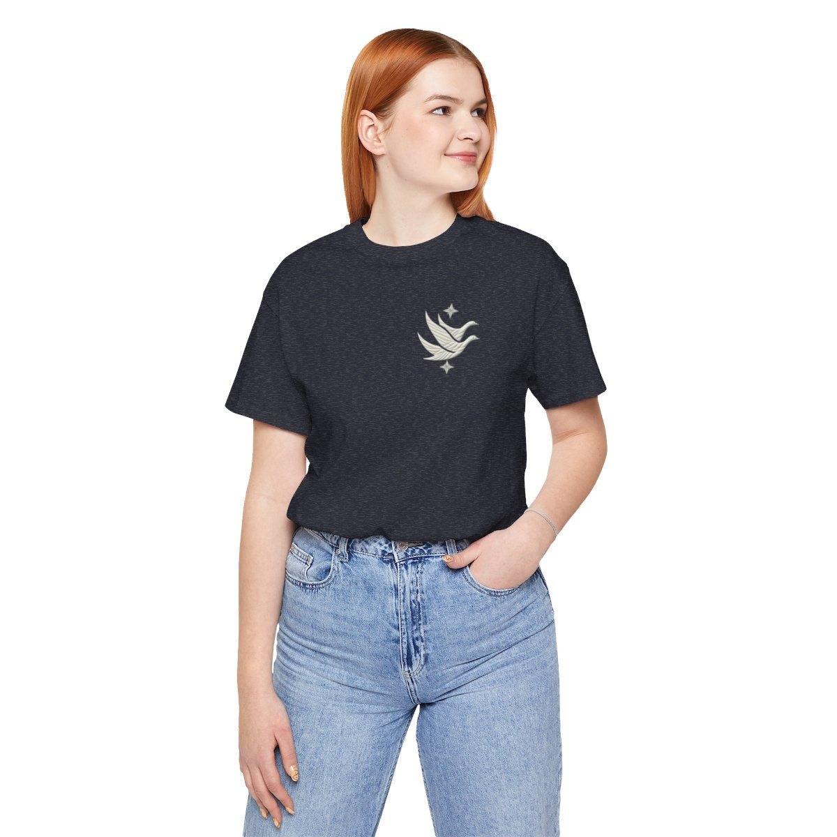 A Heather Navy T-shirt featuring two stylized white geese in flight, with outstretched wings. The geese are composed of intricate geometric patterns resembling quilt stitching. Two eight-pointed stars frame the scene, one above and one below the geese, adding a celestial element to the peaceful composition.