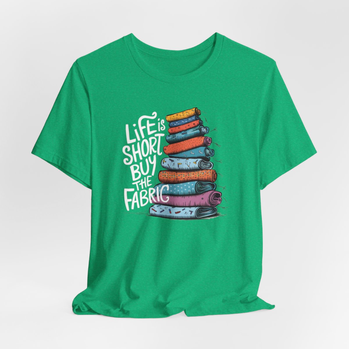 A Heather Kelly fun T-Shirt with the phrase Life is Short, Buy the Fabric with the label 'Life is Short, Buy the Fabric' next to a graphic of a fun pile of fabric