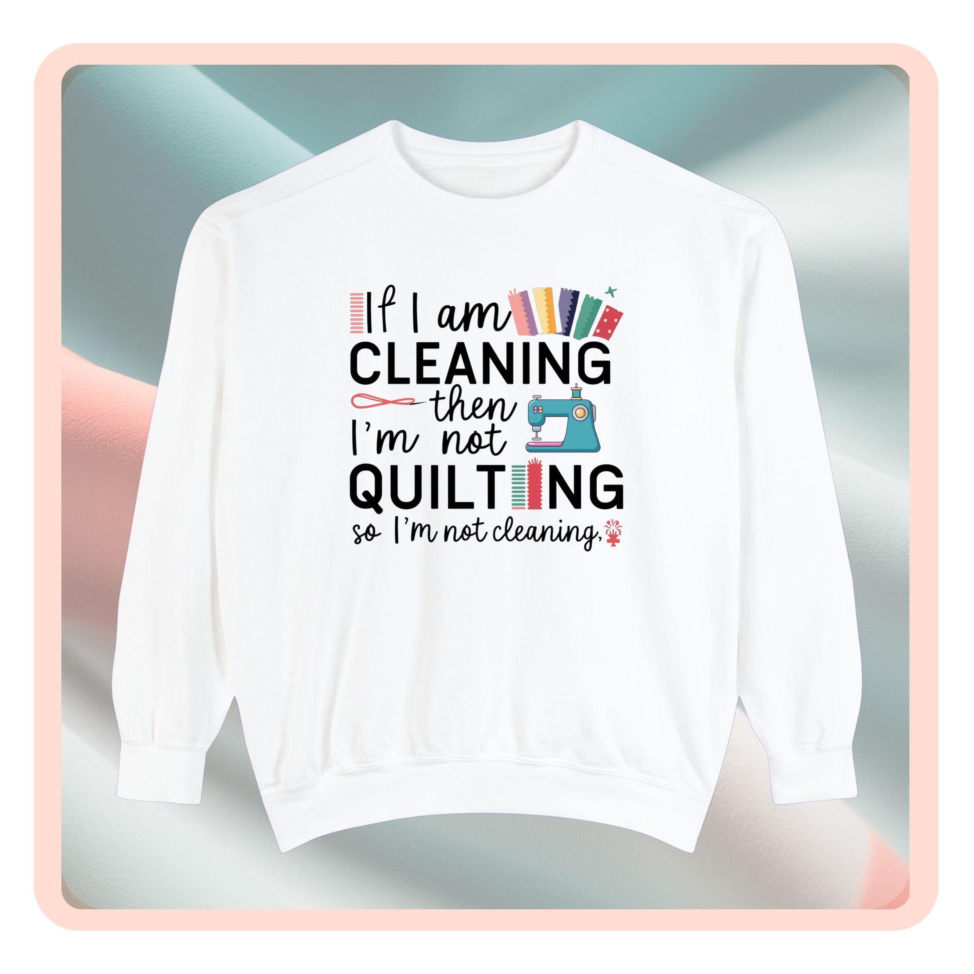 A funny Sweatshirt with the phrase If I am Cleaning then I'm not Quilting in a bold and cheerful font with images of quilting icons and supplies