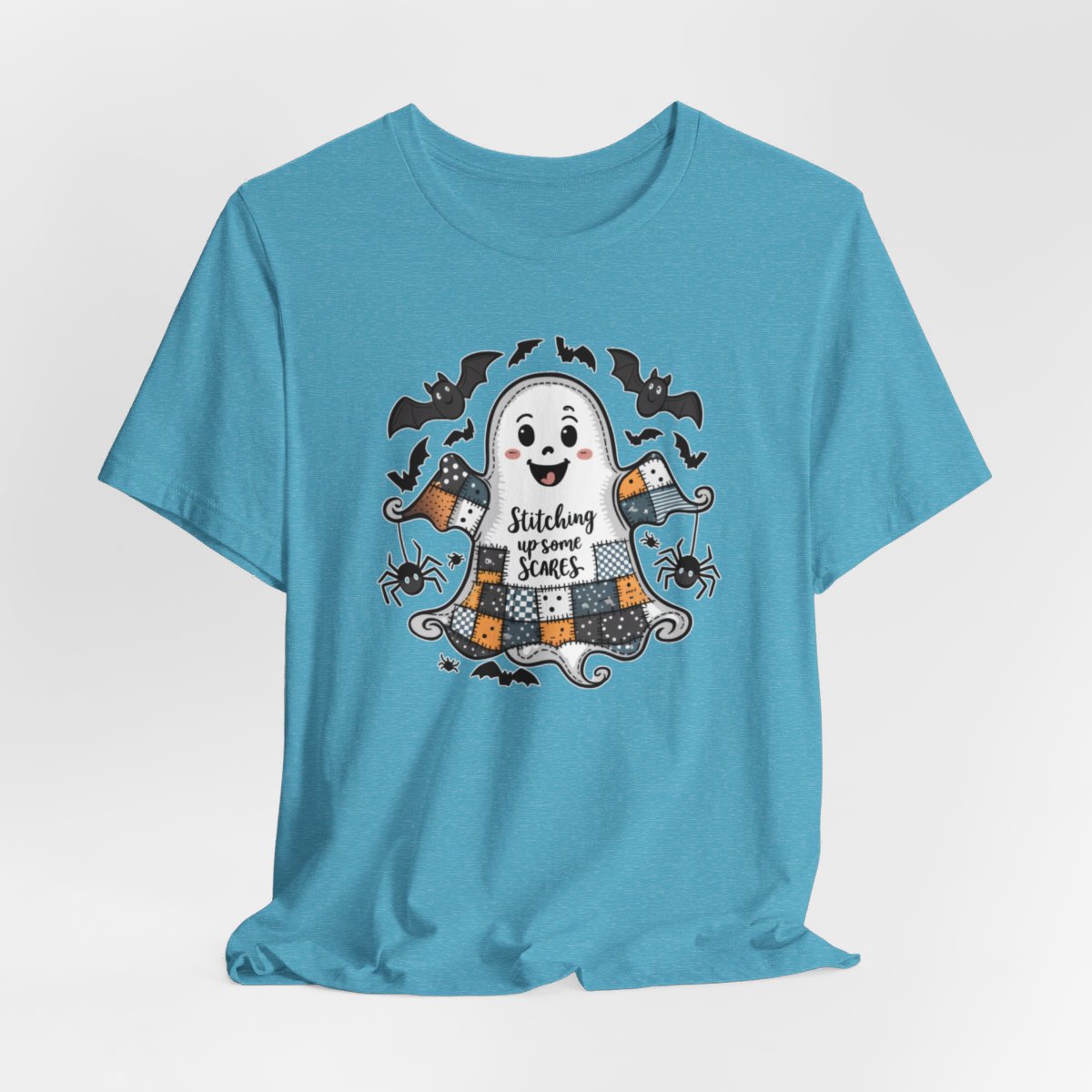 A Heather Aqua Halloween Quilting T-Shirt featuring a smiling ghost with quilted patchwork body. Halloween-themed quilt patterns. Cute bats and spiders around ghost. Text reads "Stitching up some Scares". Ideal for quilters who enjoy Halloween themes.