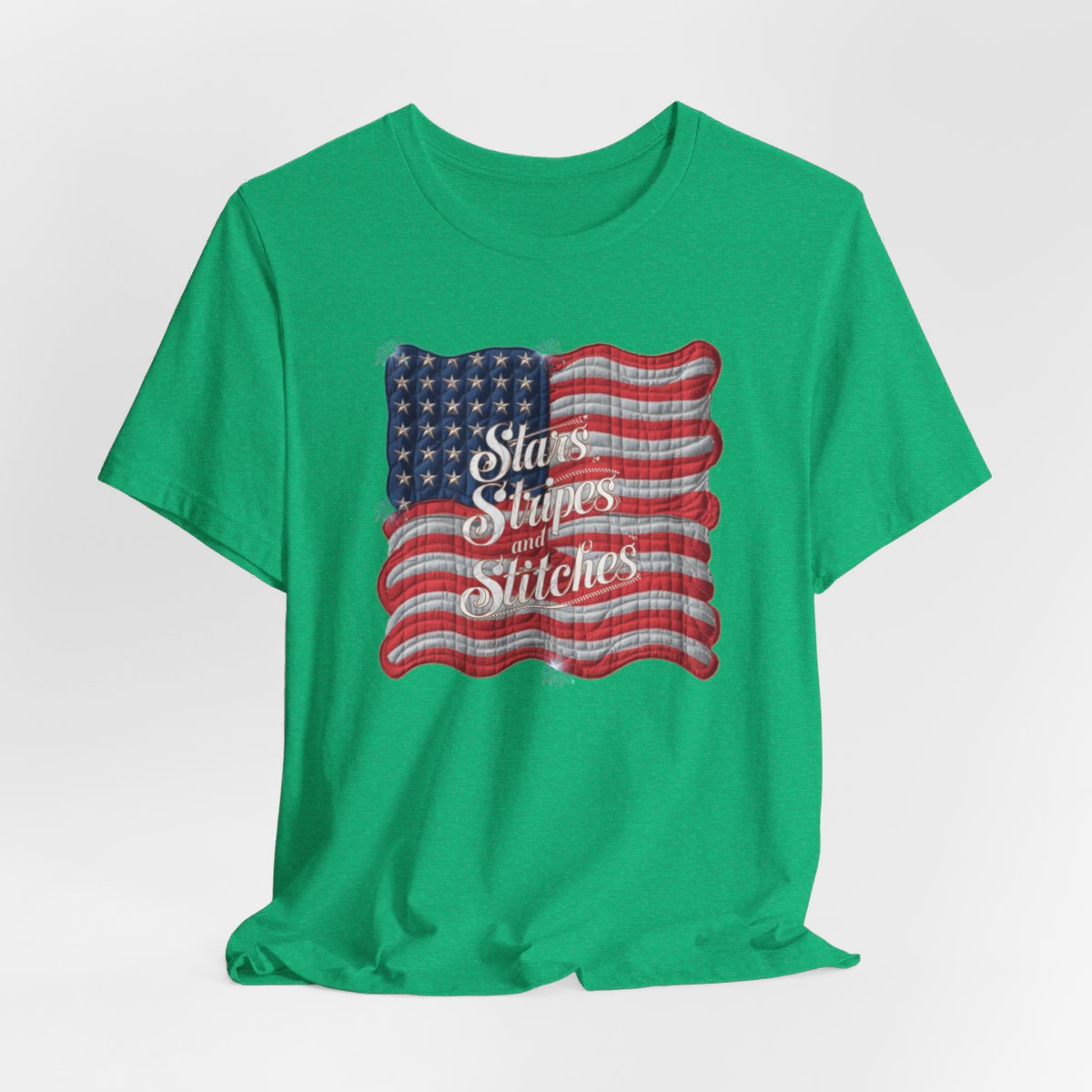 A Heather Kelly T-shirt featuring quilted American flag design with text "Stars Stripes and Stitches" overlaid in stylized, patriotic font. Fireworks accent the corners.