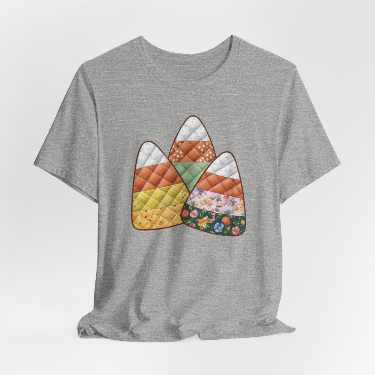 An Athletic Heather Halloween Quilting T-Shirt featuring three large candy corn shapes made of quilted fabrics with various patterns. Each candy corn section features different quilting motifs in autumn colors. Playful take on Halloween candy and quilting craft.