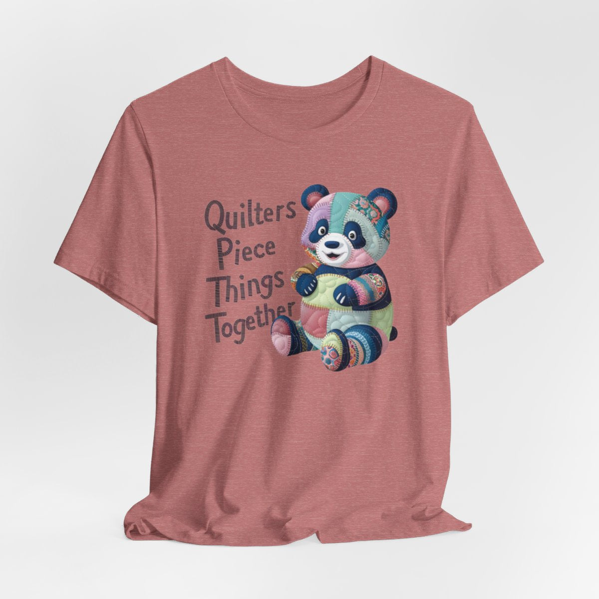 A Heather Mauve fun T-Shirt with the phrase Quilters Piece Things Together with a patchwork panda design . The panda is made of colorful fabric scraps stitched together, creating a whimsical and crafty appearance. Perfect for quilting enthusiasts with a sense of humor.