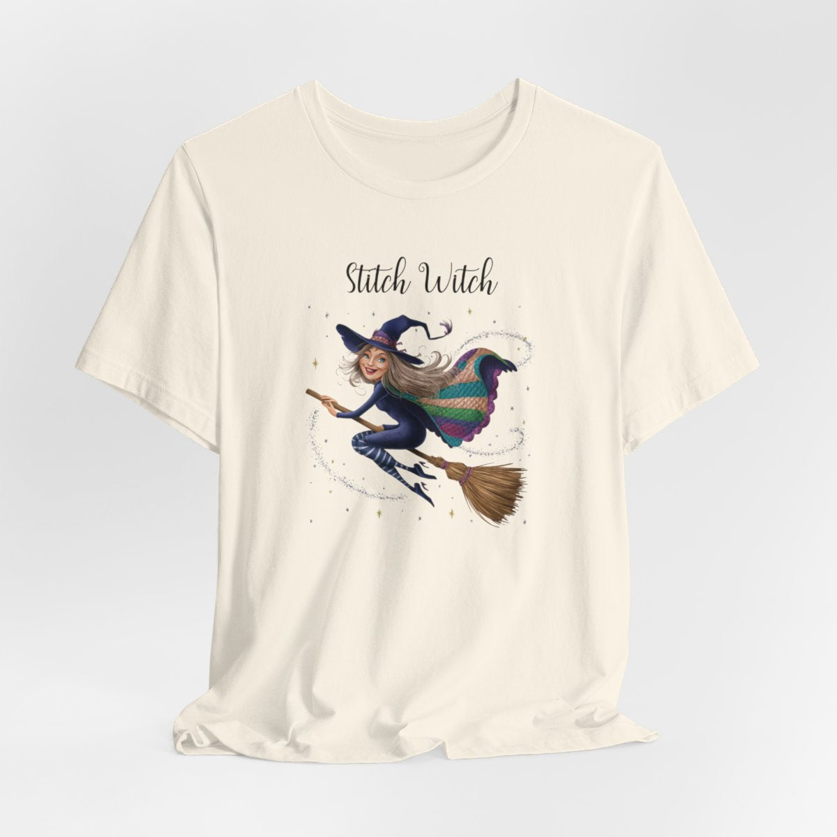 A Natural Halloween Quilting T-Shirt featuring a witch riding broomstick on t-shirt design. Colorful patchwork quilt cape with various patterns. Sparkling magic and stars. Text reads "Stitch Witch". Ideal for quilters who enjoy magical themes.