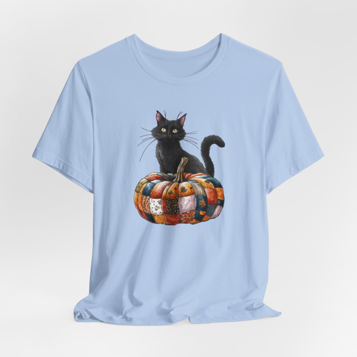 A Baby Blue Halloween Quilting T-Shirt featuring a black cat sitting on colorful patchwork quilt pumpkin. Cat has yellow eyes and long whiskers. Pumpkin features various quilt patterns in autumn colors. Halloween-themed t-shirt design for quilting enthusiasts.