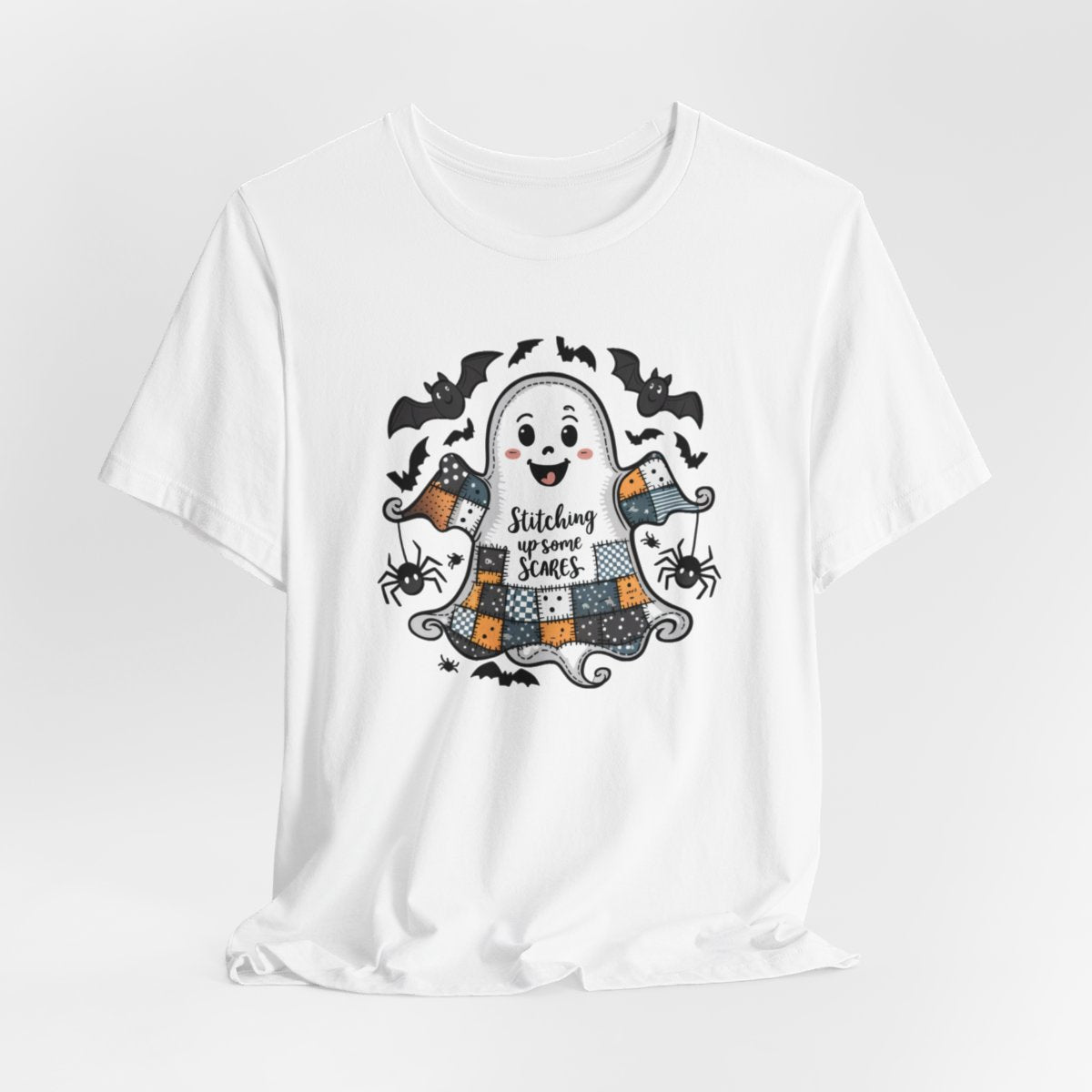 A White Halloween Quilting T-Shirt featuring a smiling ghost with quilted patchwork body. Halloween-themed quilt patterns. Cute bats and spiders around ghost. Text reads "Stitching up some Scares". Ideal for quilters who enjoy Halloween themes.