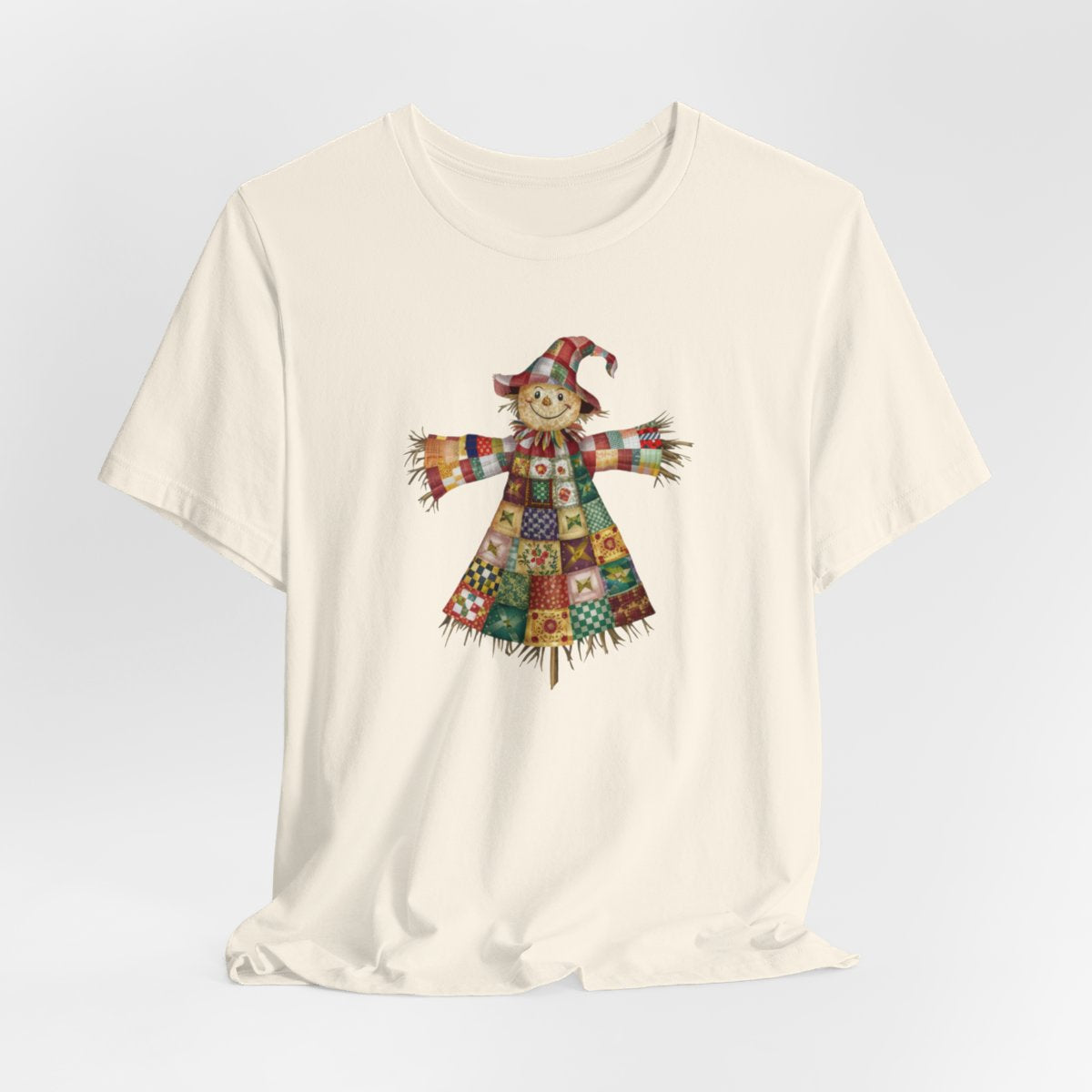 A Natural thanksgiving  quilting t-shirt featuring a smiling scarecrow made entirely of colorful quilt patterns. Wearing a patchwork hat and clothes with various quilt designs. Straw details on hands and neck. Cheerful autumn-themed illustration celebrating quilting craft.