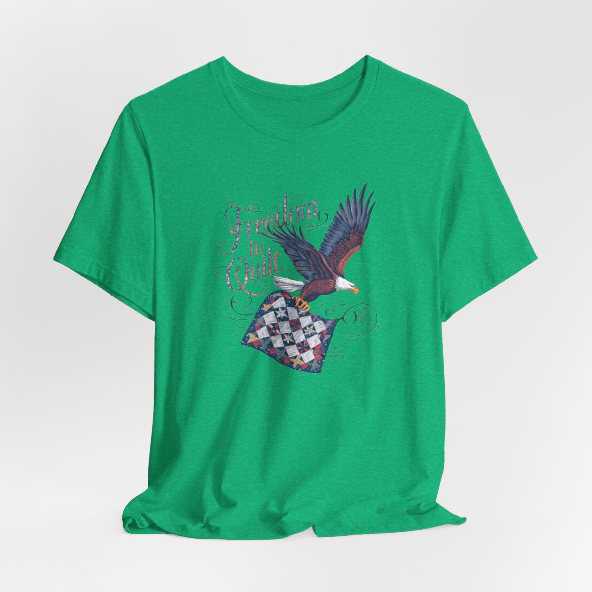 A Heather Kelly T-shirt with detailed illustration of a bald eagle in flight, carrying a patchwork quilt. Text reads "Freedom to Quilt" in an ornate, patriotic font.