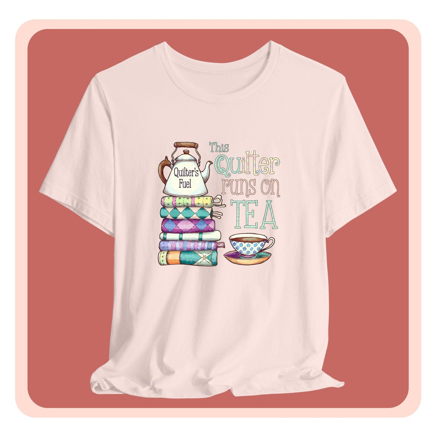 A t-shirt featuring a whimsical design of a stack of patchwork quilts with a teapot labeled 'Quilter's Fuel' and the phrase 'This Quilter Runs on Tea,' ideal for tea-loving quilters.