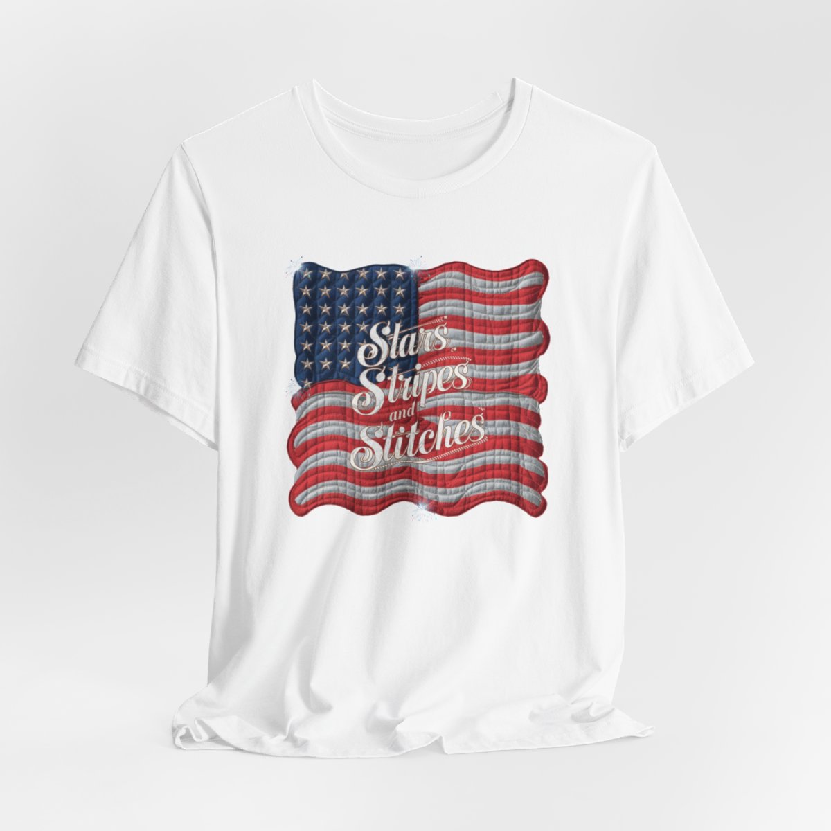 A White T-shirt featuring quilted American flag design with text "Stars Stripes and Stitches" overlaid in stylized, patriotic font. Fireworks accent the corners.