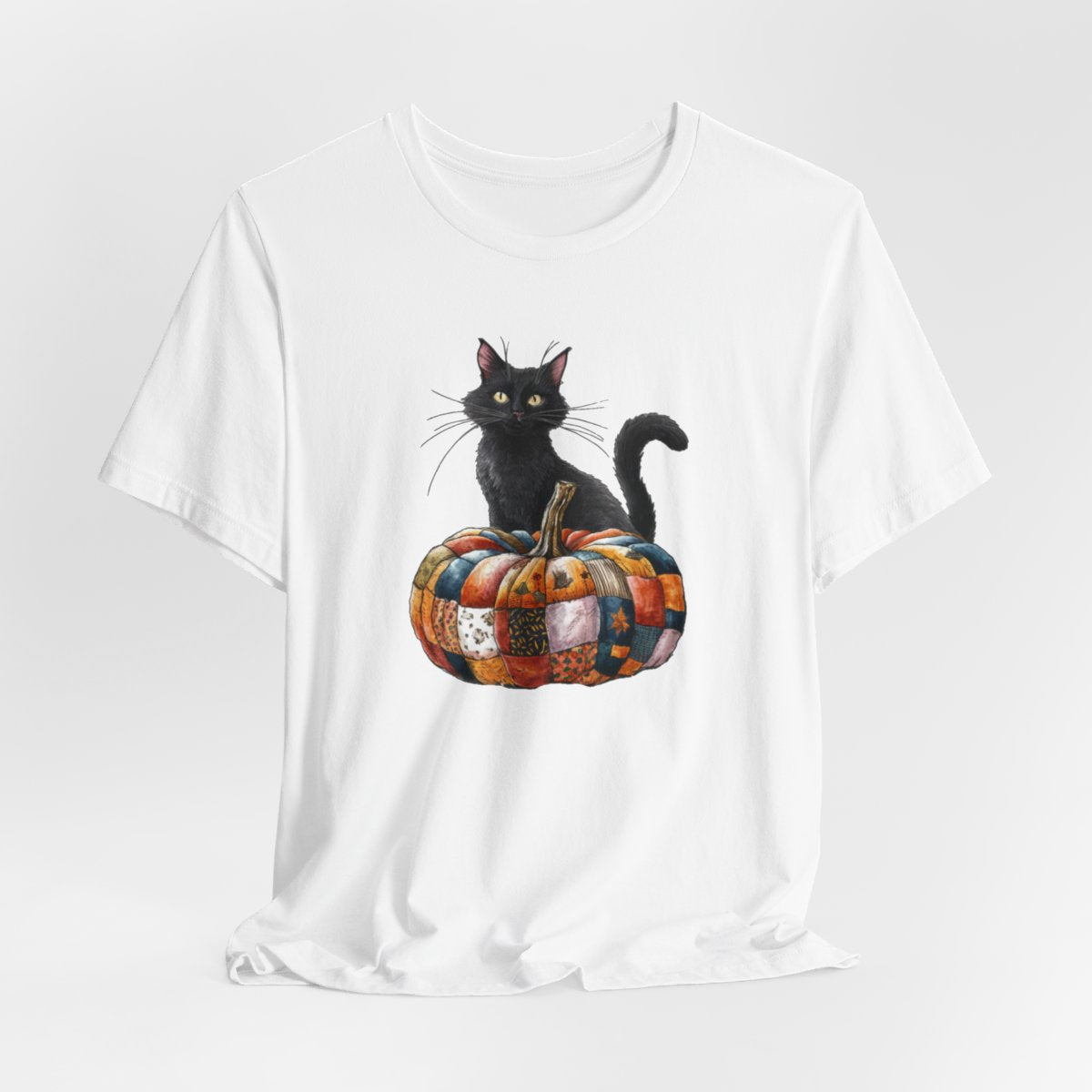 A White Halloween Quilting T-Shirt featuring a black cat sitting on colorful patchwork quilt pumpkin. Cat has yellow eyes and long whiskers. Pumpkin features various quilt patterns in autumn colors. Halloween-themed t-shirt design for quilting enthusiasts.