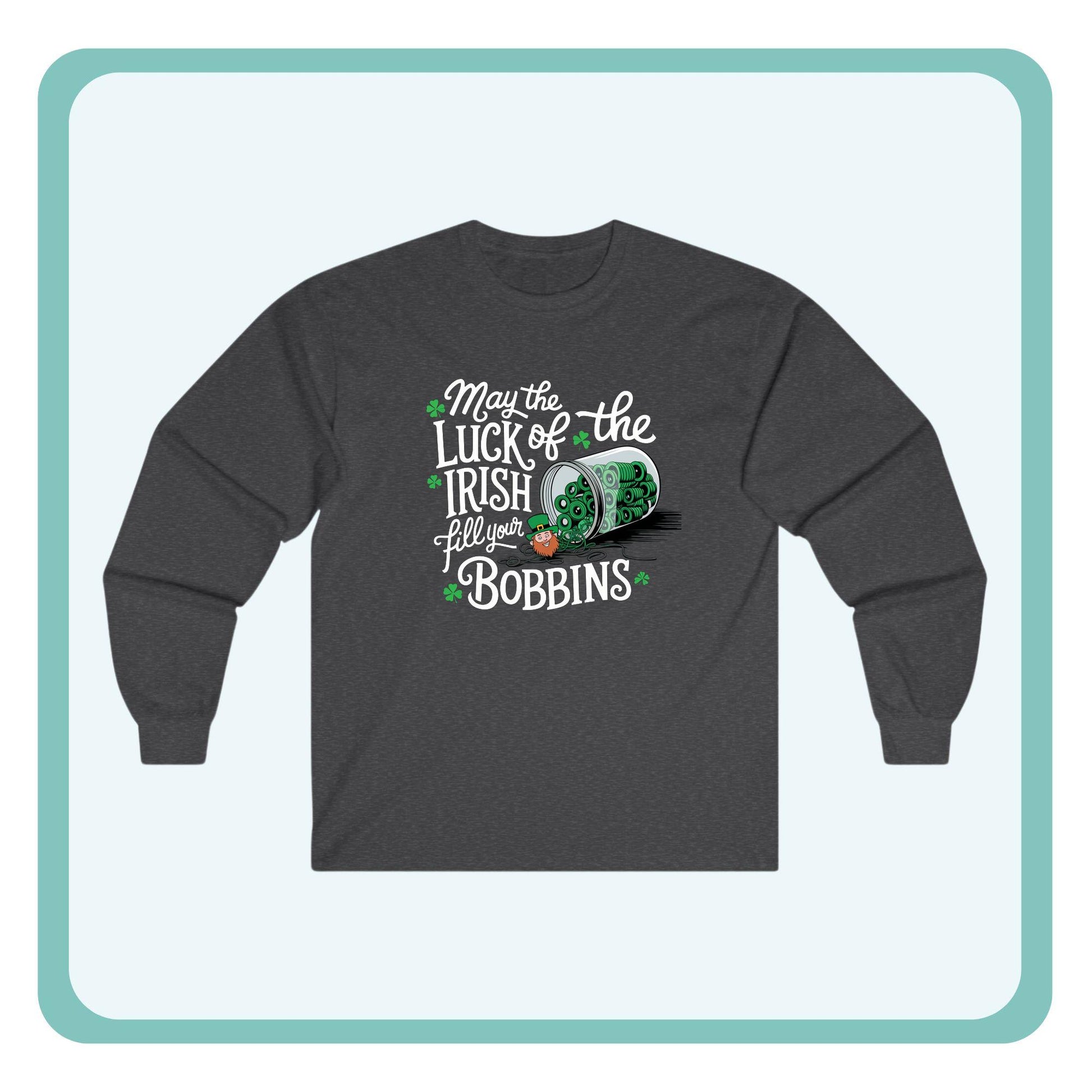 A long-sleeve t-shirt featuring a festive design with shamrocks, a spool of green thread, and the phrase 'May the Luck of the Irish Fill Your Bobbins,' perfect for quilters celebrating St. Patrick’s Day.